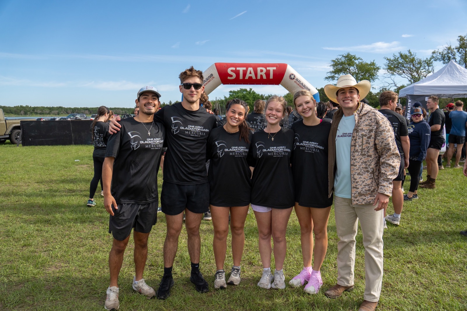 Six Gladiator Dash runners in matching black race shirts posing together in front of the start arch