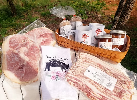 Ham steaks, bacon, sausage, Fulton Farm mugs and jars of jam laid out on a picnic blanket